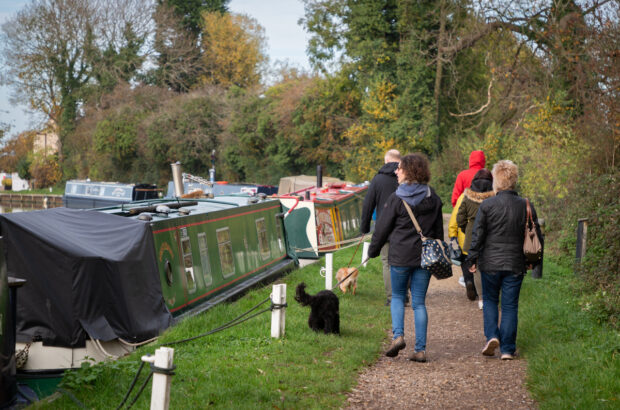 Group of people and some dogs walking along a path at Saul Junction. There are narrowboats on the left side.