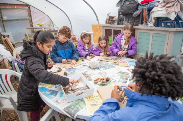 A group of kids around the table in the polytunnel, making things out of clay.