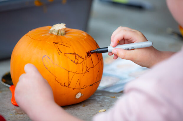 A close up of a child's hand using a sharpie to draw a design onto a pumpkin.